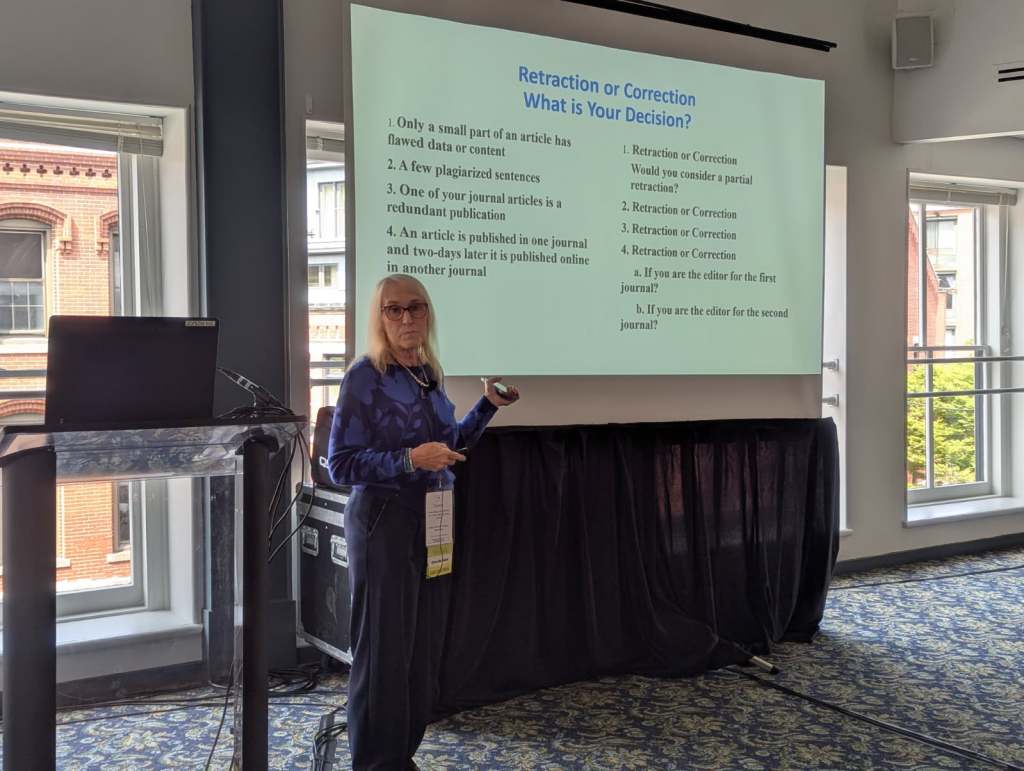 A woman presenting at a conference, standing by a projector screen displaying slides about editorial decisions on retraction and correction of articles.