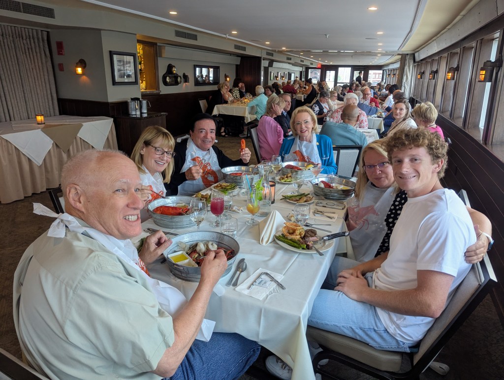 A group of diners wearing bibs gathered around a table filled with lobster and other dishes at DiMillo’s Floating Restaurant, enjoying a lively evening.