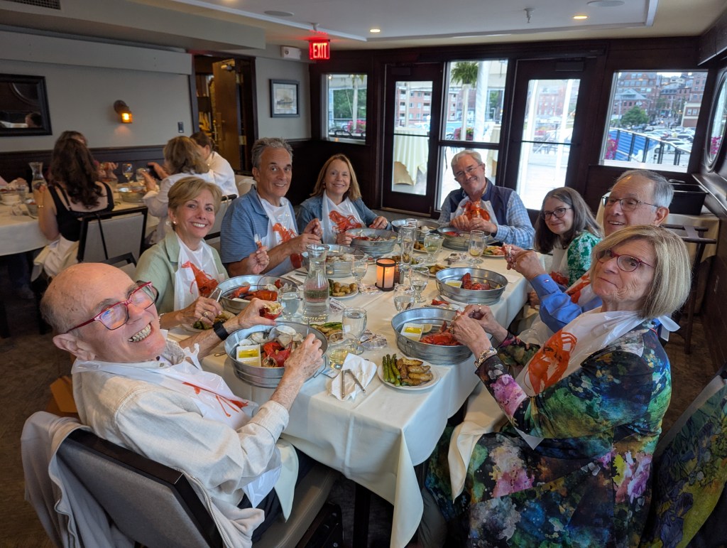 A group of diners joyfully enjoying a lobster dinner at DiMillo's Floating Restaurant, wearing lobster bibs and seated at a beautifully set table with dishes and drinks.