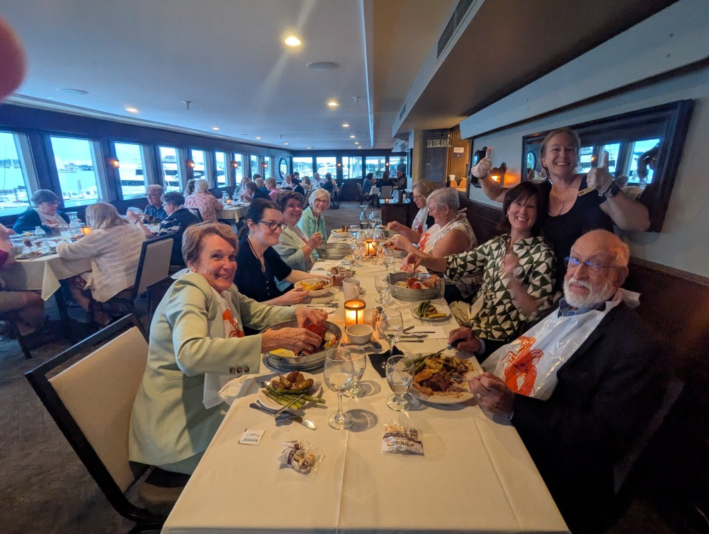 A lively dinner gathering with guests enjoying lobster and steak at DiMillo's Floating Restaurant, with laughter and camaraderie among the attendees.
