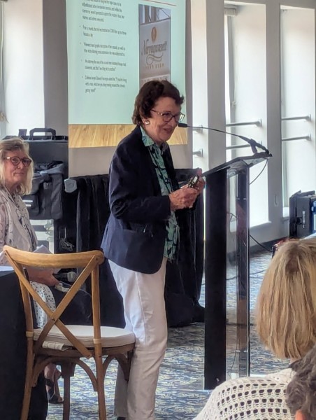 Speaker Ann Burgess presenting at the INANE Conference with audience in the background.