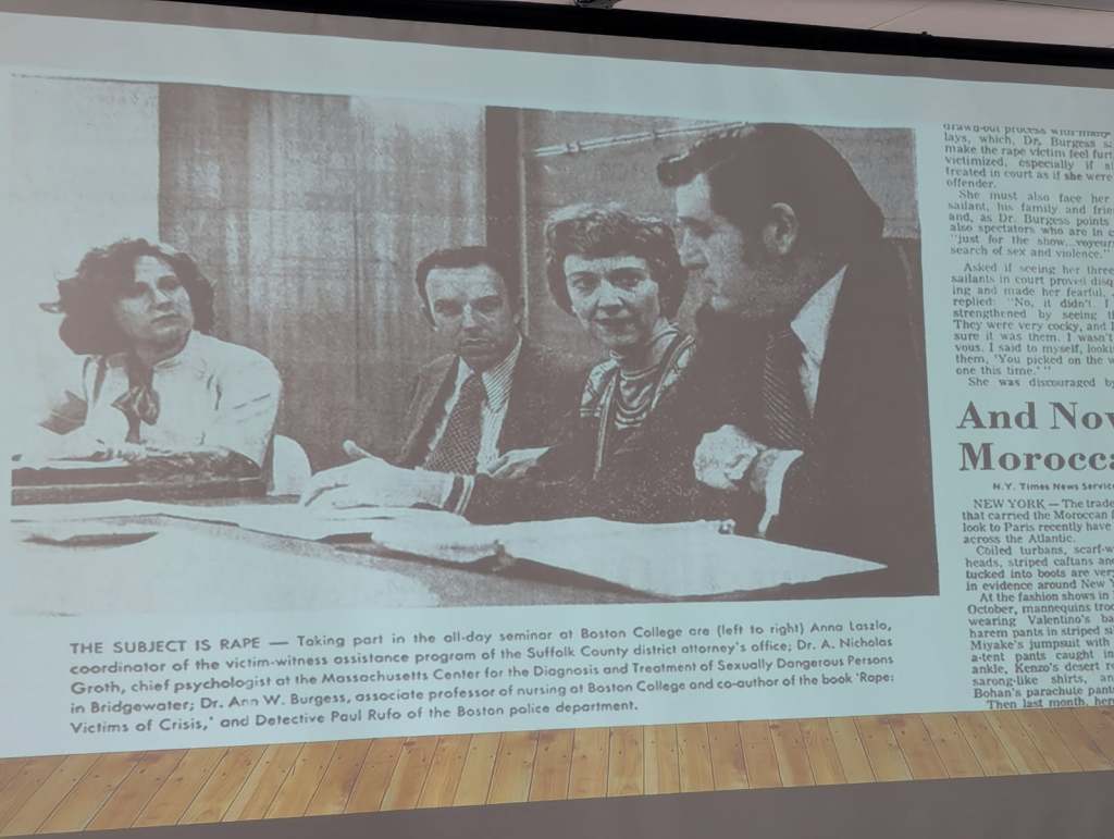 Black and white image from a seminar at Boston College discussing the topic of rape, featuring three individuals seated at a table, with text overlay detailing their roles and affiliation.