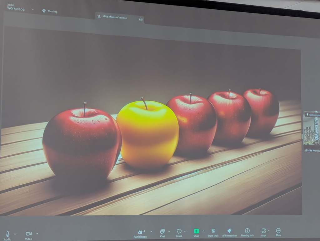 A close-up image of five apples on a wooden surface, with four red apples and one yellow apple prominently displayed.