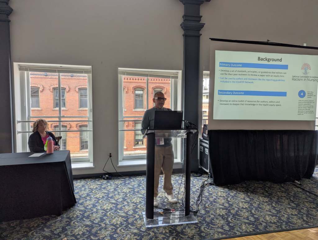 A speaker presents at a conference, discussing guidelines related to equity in nursing, with a slide visible in the background.