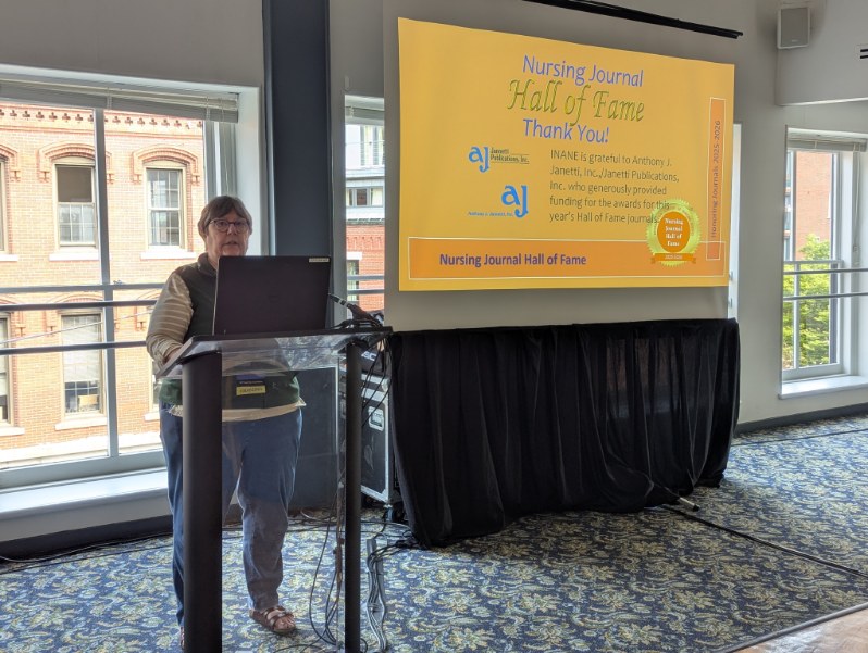 A woman speaks at a podium during the Nursing Journal Hall of Fame Ceremony, with a presentation slide thanking sponsors in the background.