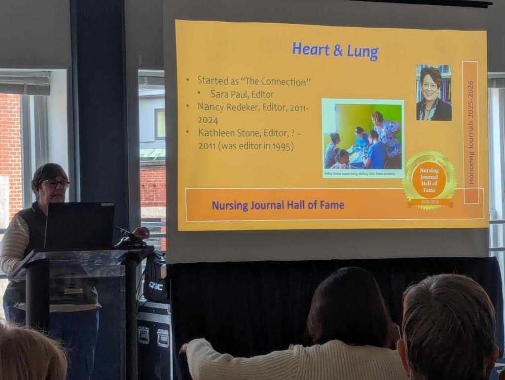 A presenter speaking at the Nursing Journal Hall of Fame Ceremony, with a presentation slide showing editors and a photo of nursing students, in a conference setting.