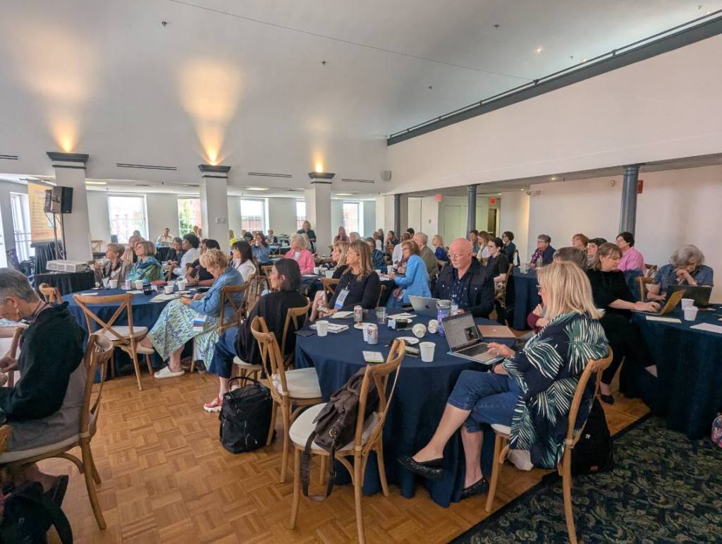 Audience members attentively participating in the Nursing Journal Hall of Fame Ceremony at the INANE Conference, seated at tables with laptops and refreshments.