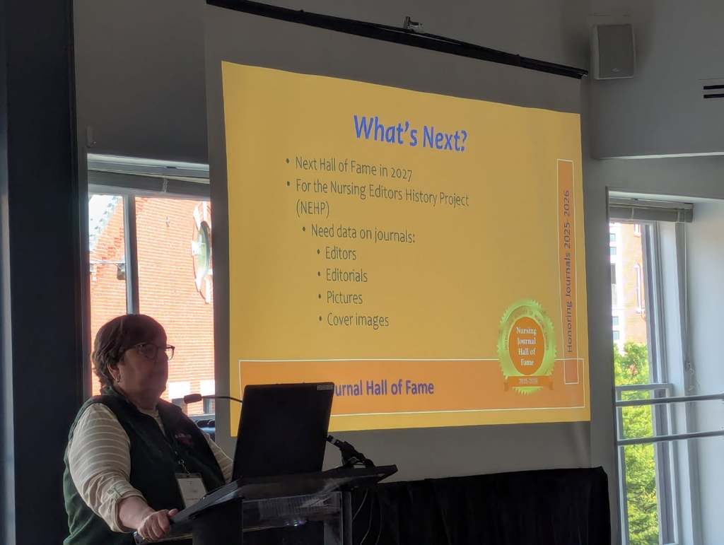 A speaker presenting at the Nursing Journal Hall of Fame ceremony, with a projector screen displaying information about future plans for the event.
