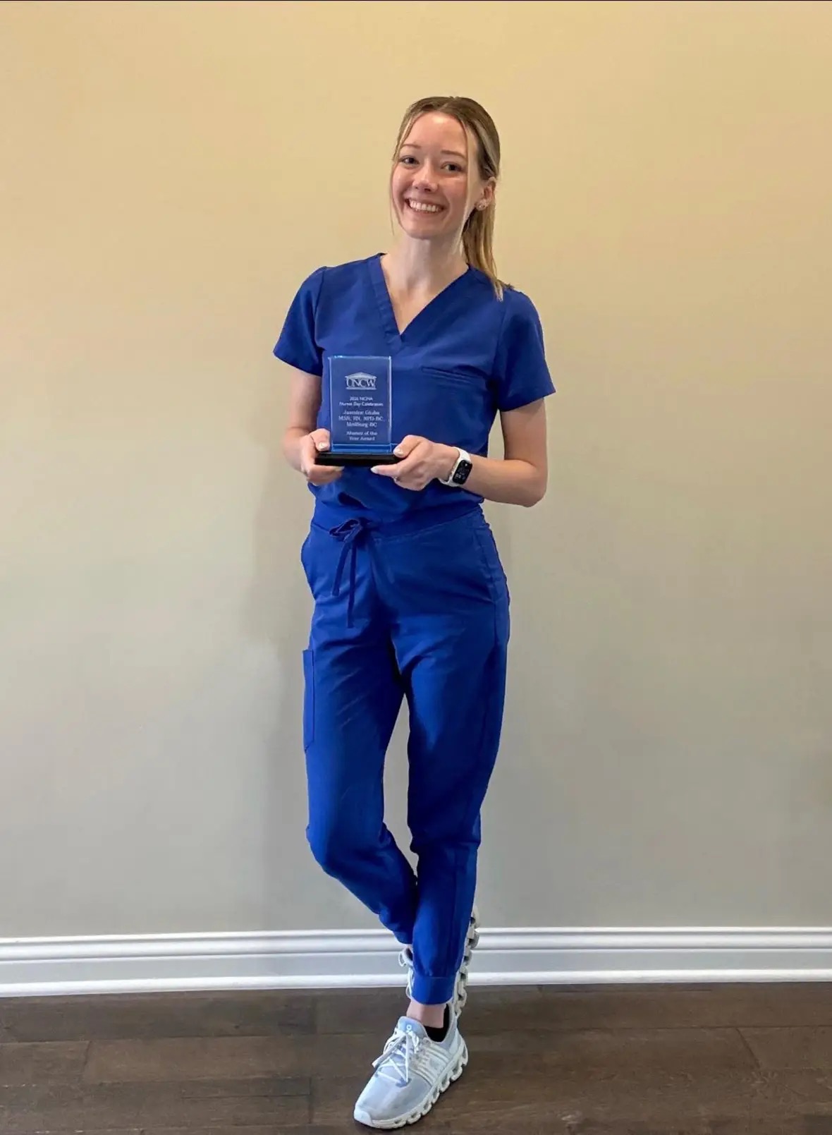 Jasmine Gluba in blue scrubs holding her University of North Carolina Wilmington Alumni of the Year Award.